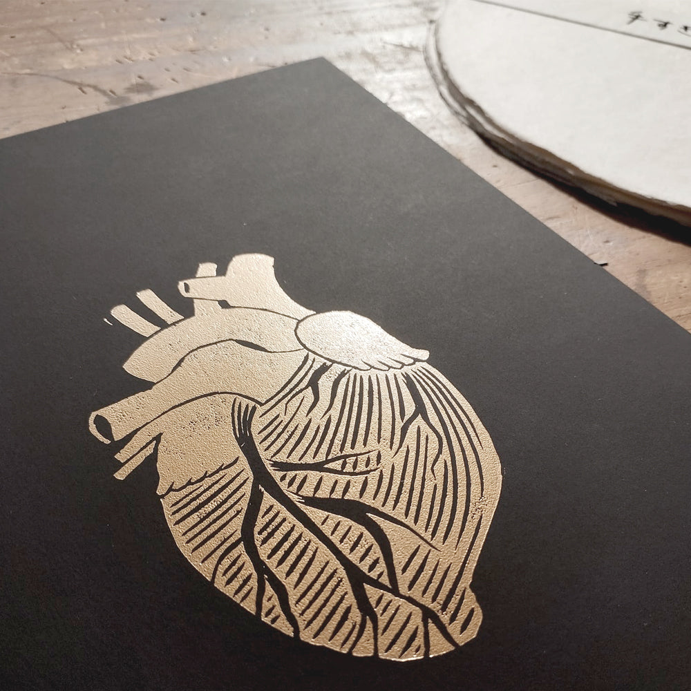 Black paper with a print of a gold metallic heart on a wooden surface