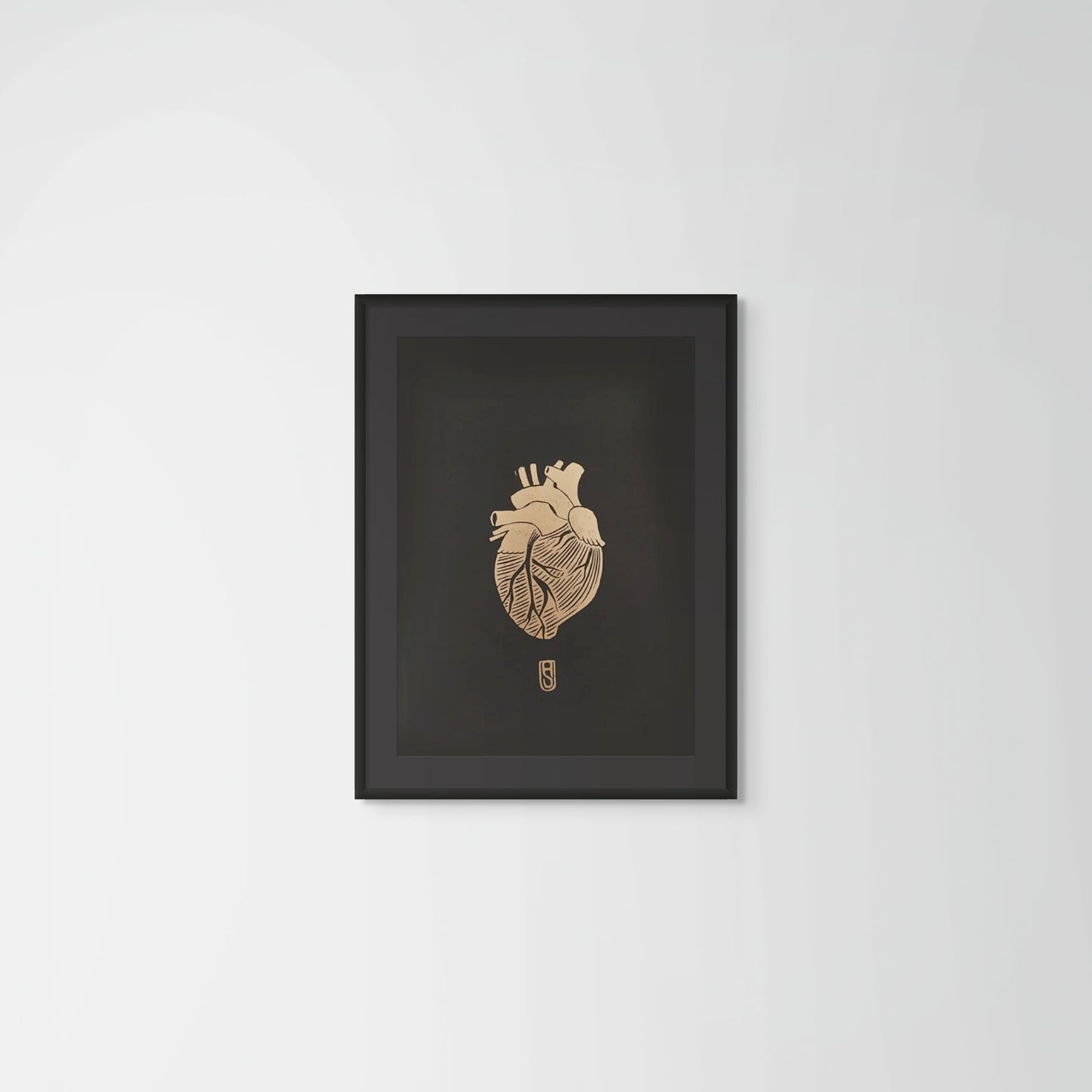 Framed artwork of a detailed anatomical heart in gold on black paper on a plain wall background