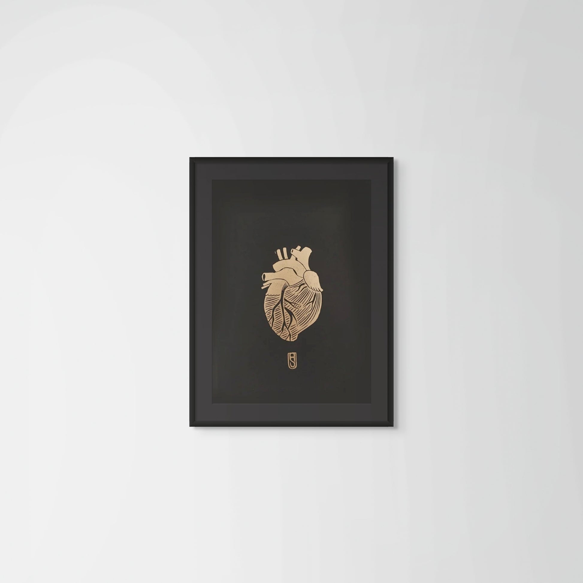 Framed artwork of a detailed anatomical heart in gold on black paper on a plain wall background