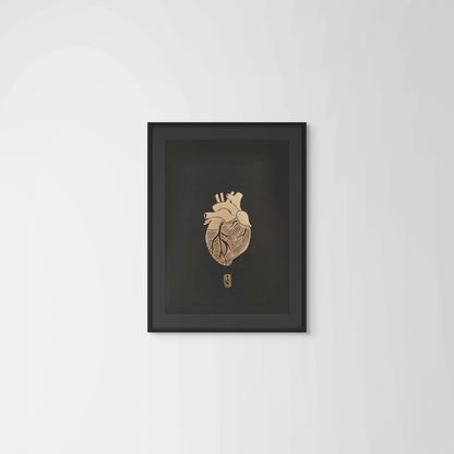 Framed artwork of a detailed anatomical heart in gold on black paper on a plain wall background