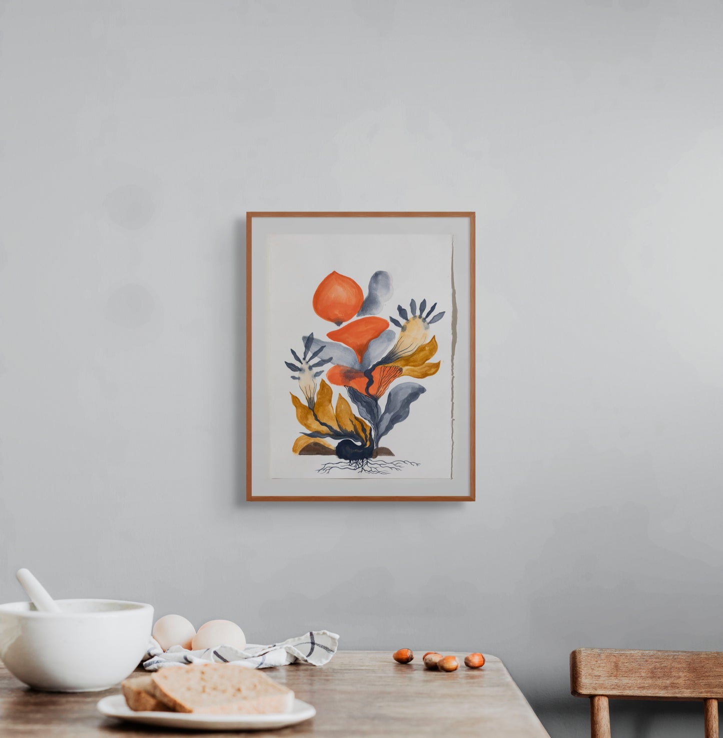 Framed floral artwork on a gray wall above a wooden table with a bowl and bread.